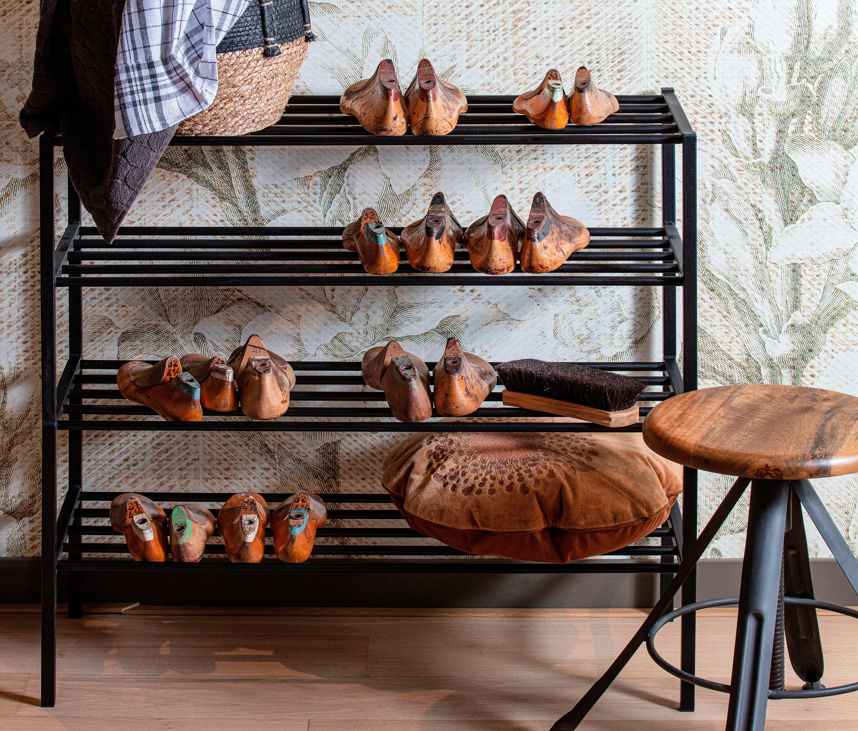 Schwarzes Metall-Schuhregal mit vier Regalböden voller hölzerner Entenschuhe, einer Bürste und einem braunen Kissen.