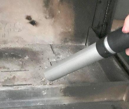 Eine Aschesauger-Düse saugt Asche aus einem Kamin.