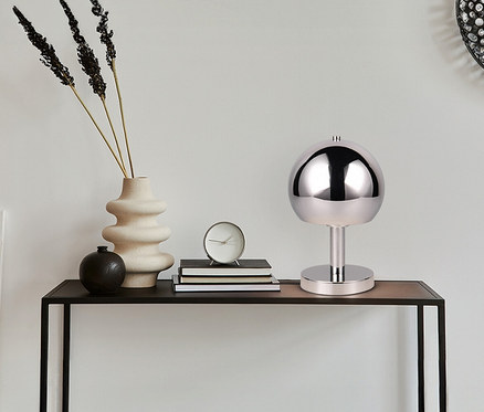 Auf einem Tisch stehen eine Trio Tischleuchte »Boccia«, eine Vase mit Pflanzen und eine Uhr.
