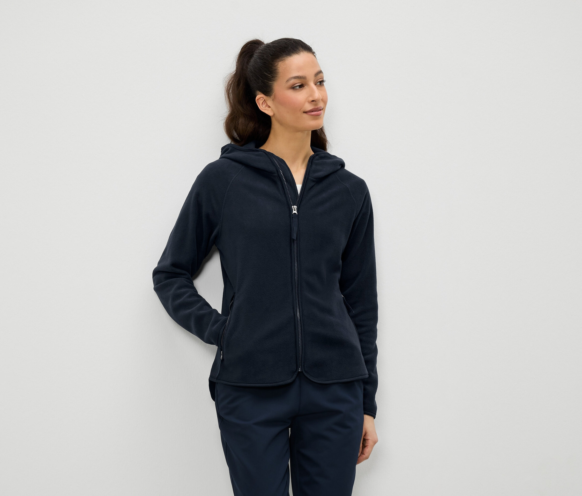 Frau trägt eine dunkelblaue Fleecejacke mit Kapuze und Reißverschluss und dunkelblaue Hosen.