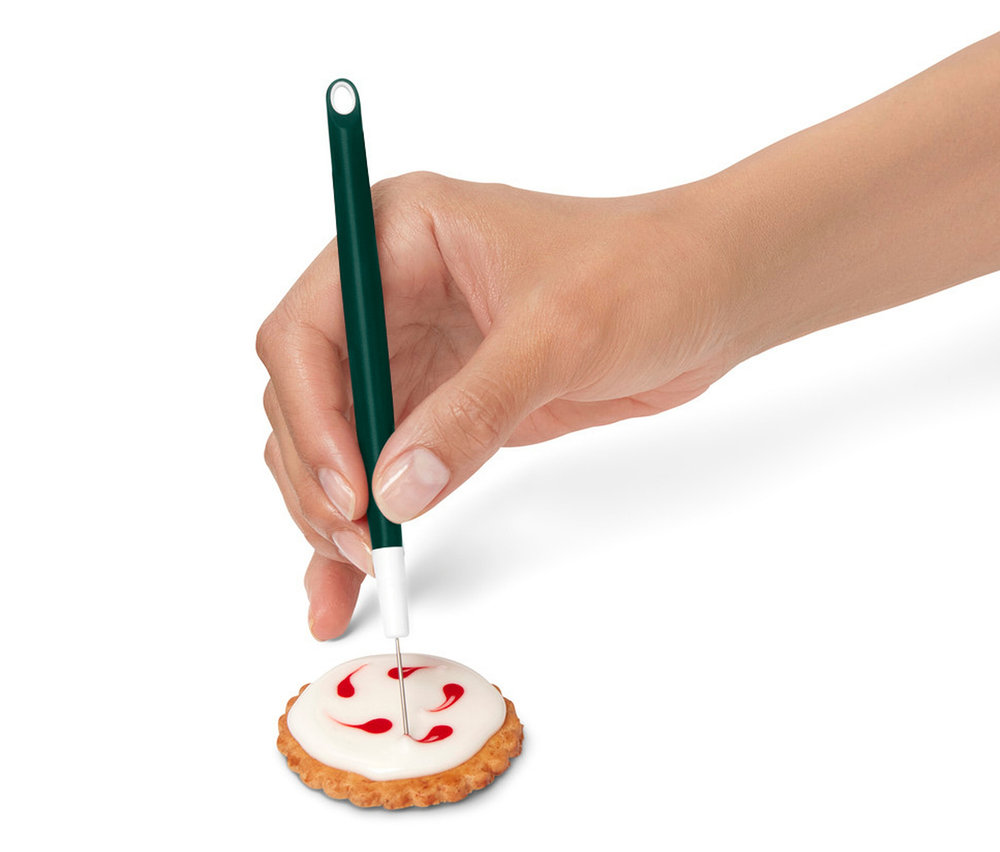 Eine Hand verziert einen Keks mit Zuckerguss mit einem grünen Dekorationsstift.