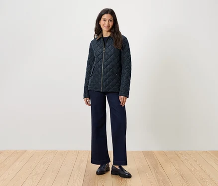 Frau steht und trägt eine gesteppte Jacke, Jeans und Slipper.