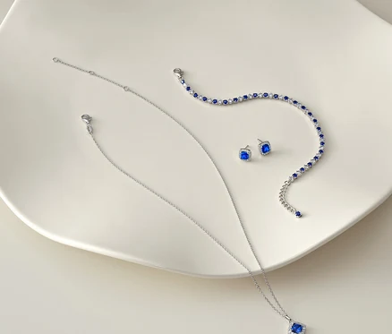 Silberne Halskette, Armband und Ohrringe mit blauen Steinen auf weißem Hintergrund.