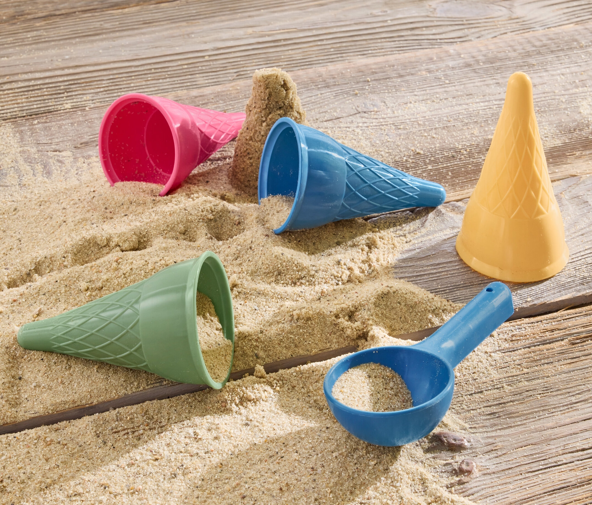 Eis-Sandformen und Sand liegen auf einer Holzoberfläche.