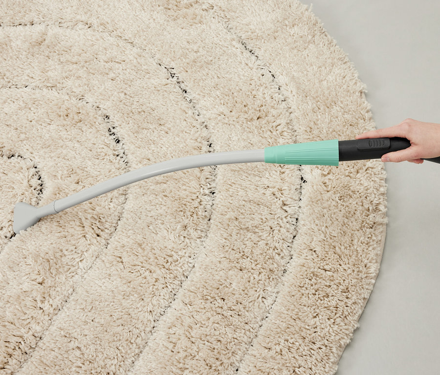 Eine Person saugt mit einem Staubsauger-Aufsatz einen runden Teppich.