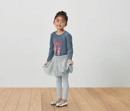 Mädchen im grauen Ballett-Outfit mit T-Shirt, Rock und Leggings.