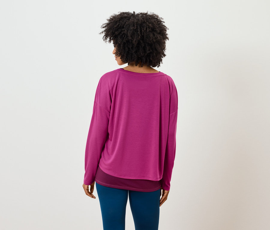 Rückansicht einer Frau mit Afro-Frisur, die ein rosafarbenes Langarmshirt und blaue Leggings trägt.