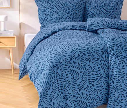 Ein blaues Bettwäsche-Set mit Blattmuster auf einem Bett mit Kopfteil. Ein Nachttisch mit Lampe steht neben dem Bett.