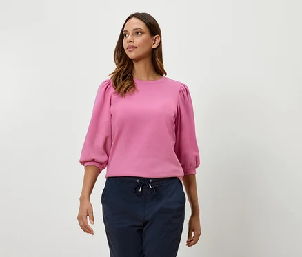 Frau trägt ein pinkes Sweatshirt mit Dreiviertel-Ballonärmeln und marineblaue Hosen.
