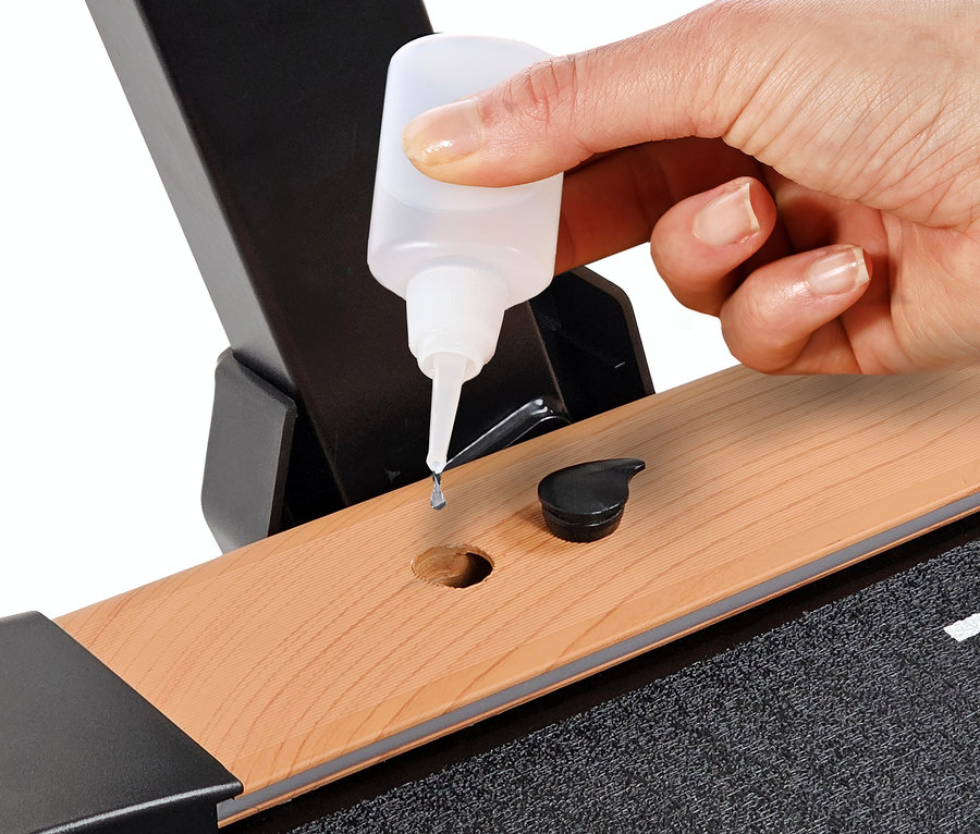 Eine Hand tropft Öl auf ein Laufband 2 in 1 in Holzoptik.