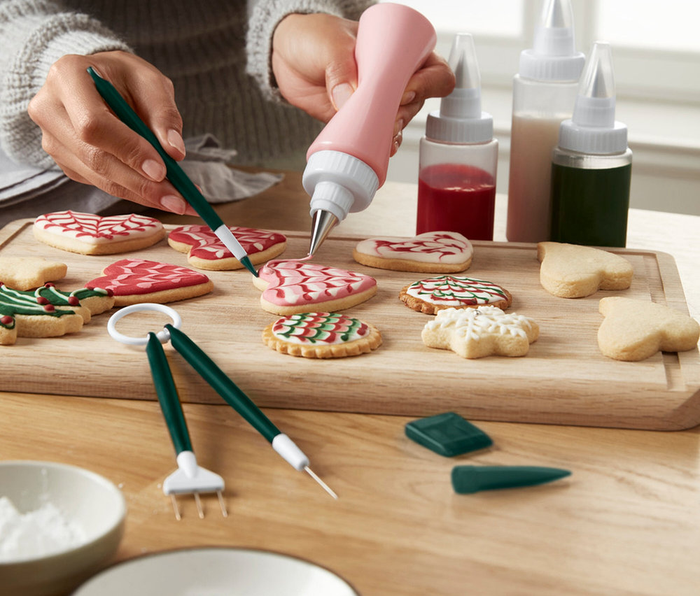 Frau verziert Lebkuchen mit Zuckerguss mit einer Spritztüte und einem Pinsel.