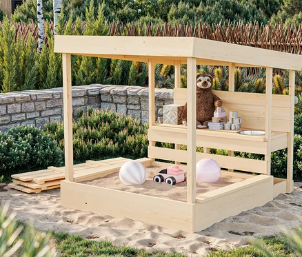 Ein hölzernes Sandhaus mit Spielzeug darin steht im Sand.