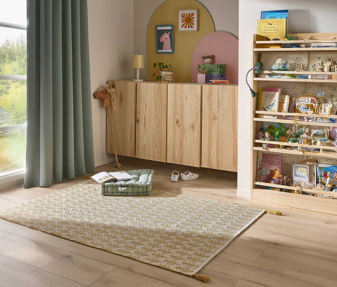 Ein Kinderzimmer mit einem Teppich, einem Sideboard und einem Bücherregal.