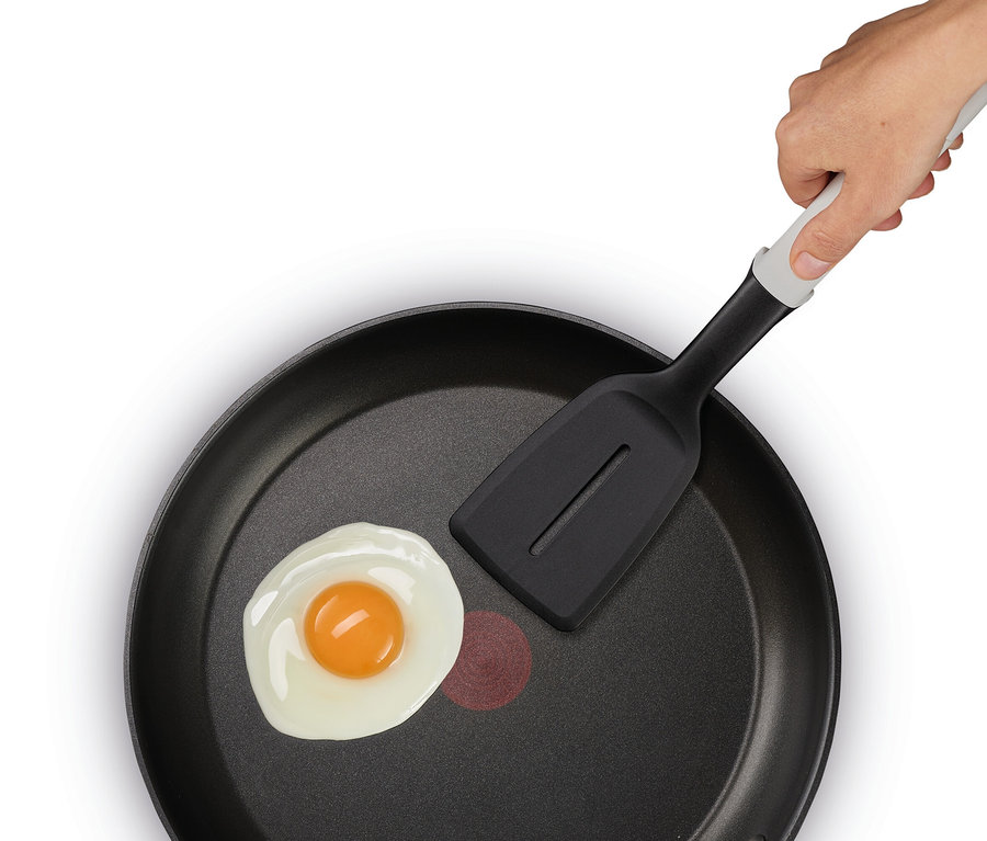 Eine Hand hält einen schwarzen Pfannenwender über ein Spiegelei in einer schwarzen Bratpfanne.