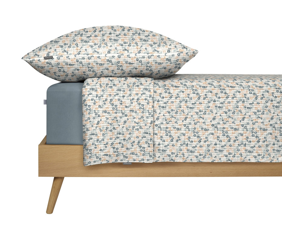 Bett mit blauem Spannbettlaken und blumengemusterter Bettwäsche mit Kissen.