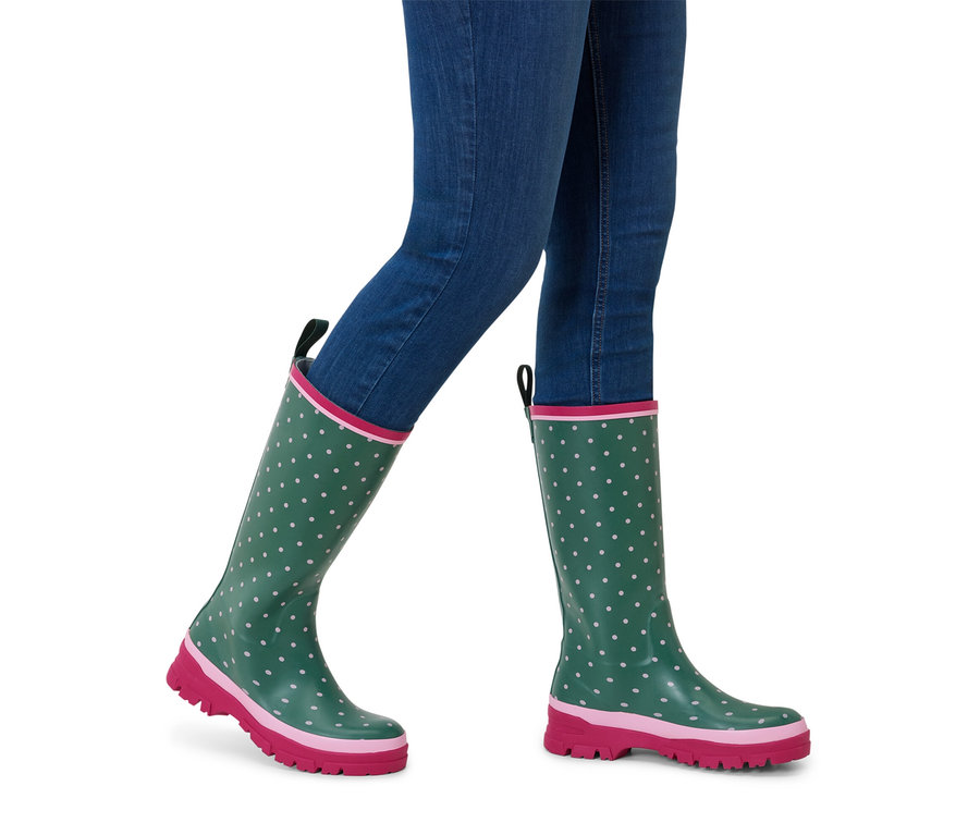 Person trägt blaue Jeans und grüne Gummistiefel mit rosa Sohle und weißen Punkten.