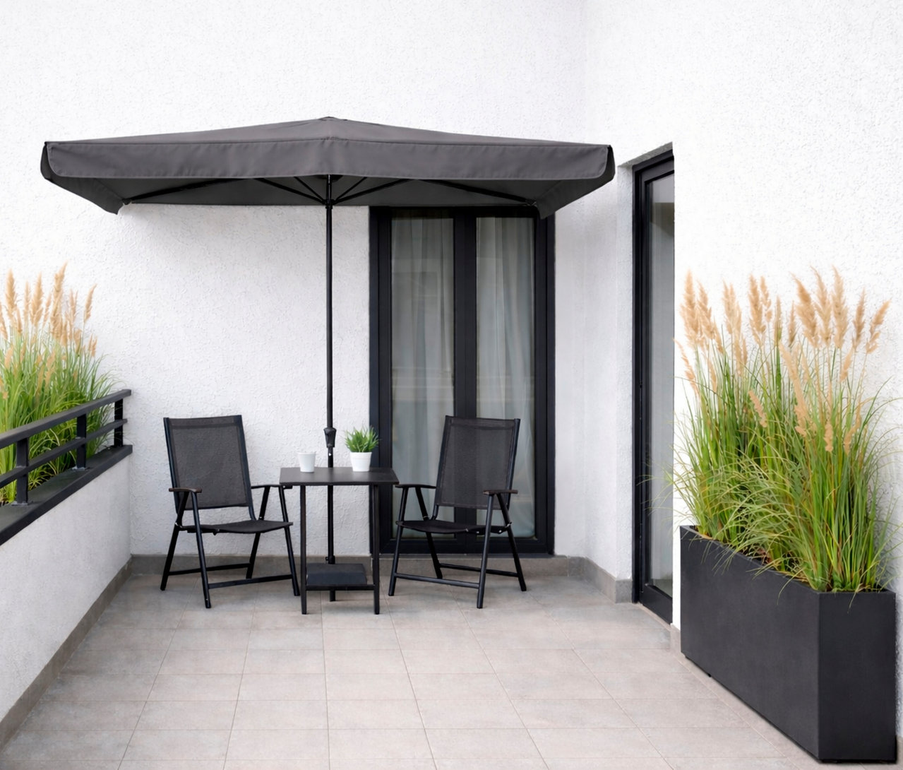 Auf einer Terrasse stehen zwei schwarze Stühle und ein Tisch mit einem Sonnenschirm darüber.