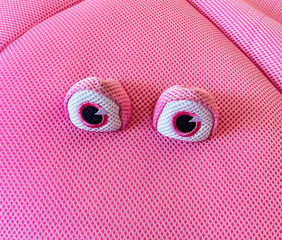 Nahaufnahme von zwei rosa Spielzeugaugen auf einem pinkfarbenen, texturierten Untergrund.