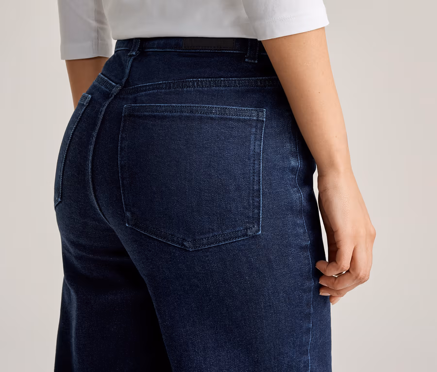 Nahaufnahme einer Frau in dunkelblauen Jeans und weißem Oberteil, von hinten fotografiert.