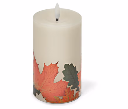 Eine cremefarbene, zylindrische LED-Kerze mit Herbstlaubdekor steht auf einem weißen Untergrund.