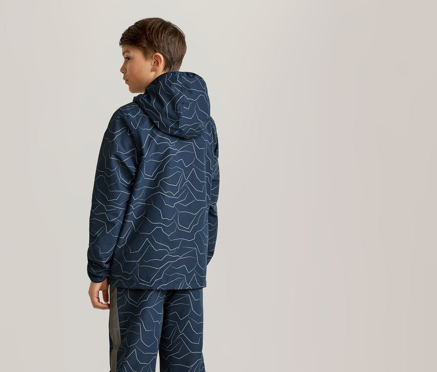 Ein Junge steht in einem marineblauen Hoodie mit Kapuze und passender Hose mit weißem Bergmuster.