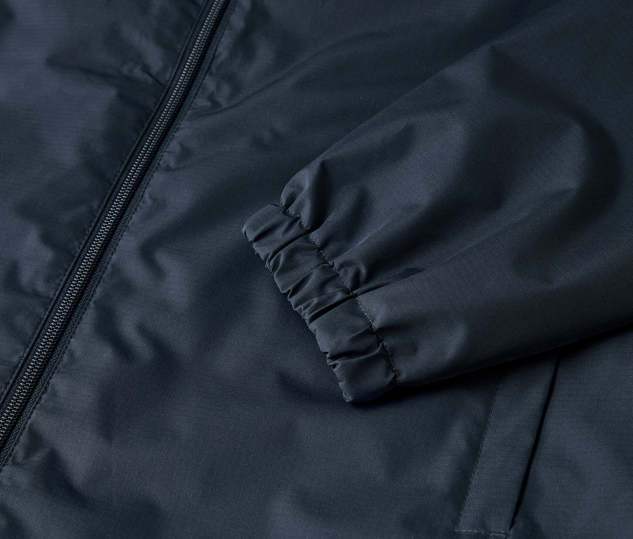 Detailansicht einer marineblauen Jacke mit Reißverschluss und elastischen Bündchen.