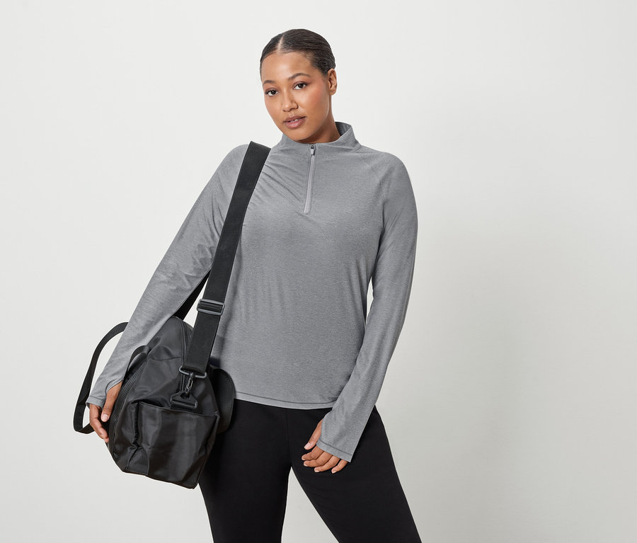 Frau trägt ein graues, langärmliges Oberteil und eine schwarze Sporttasche über ihrer Schulter.