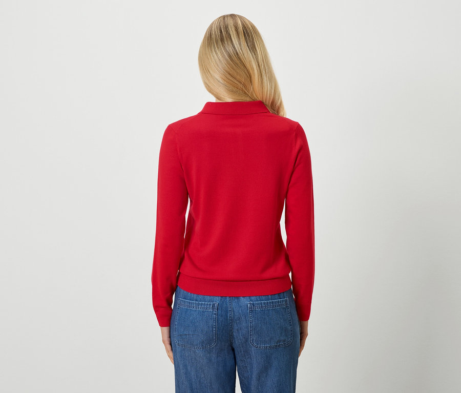 Rückansicht einer Frau mit blonden Haaren, die einen roten Pullover und blaue Jeans trägt.