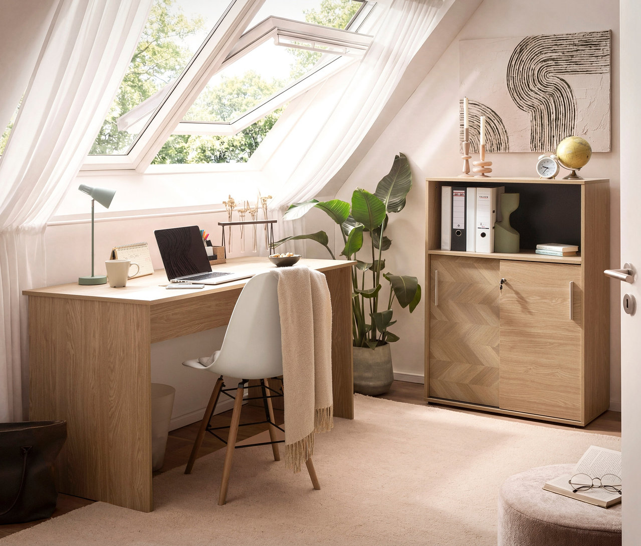 Ein Arbeitszimmer mit Schreibtisch, Laptop, Stuhl mit Tuch, Schrank, Zimmerpflanze und Dachfenster.