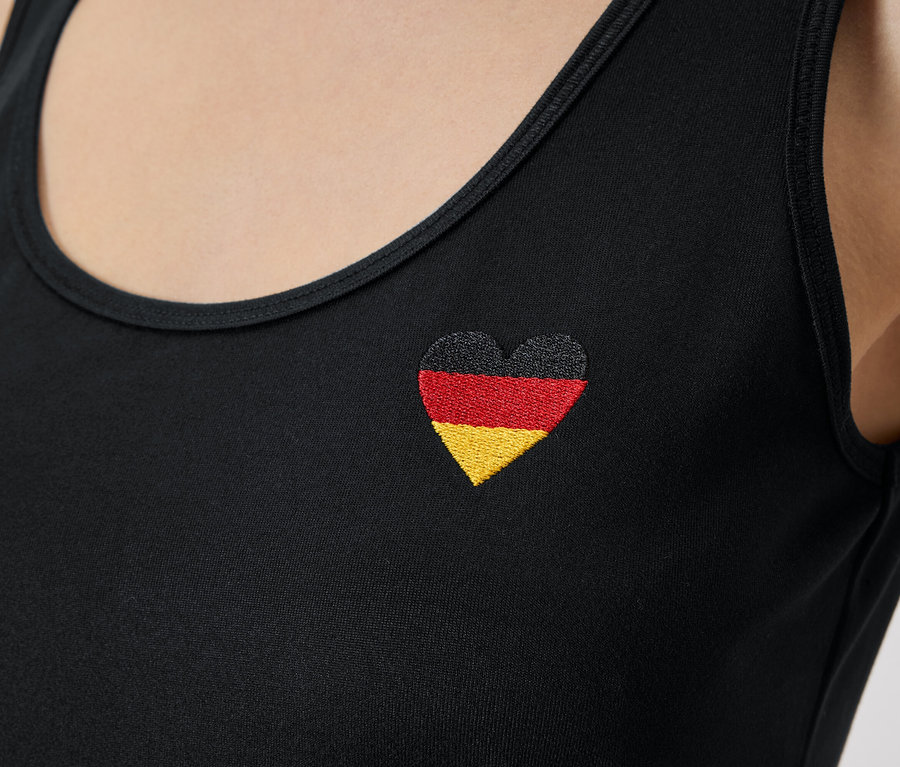 Nahaufnahme einer Person, die ein schwarzes Tanktop mit einer herzförmigen deutschen Flagge trägt.