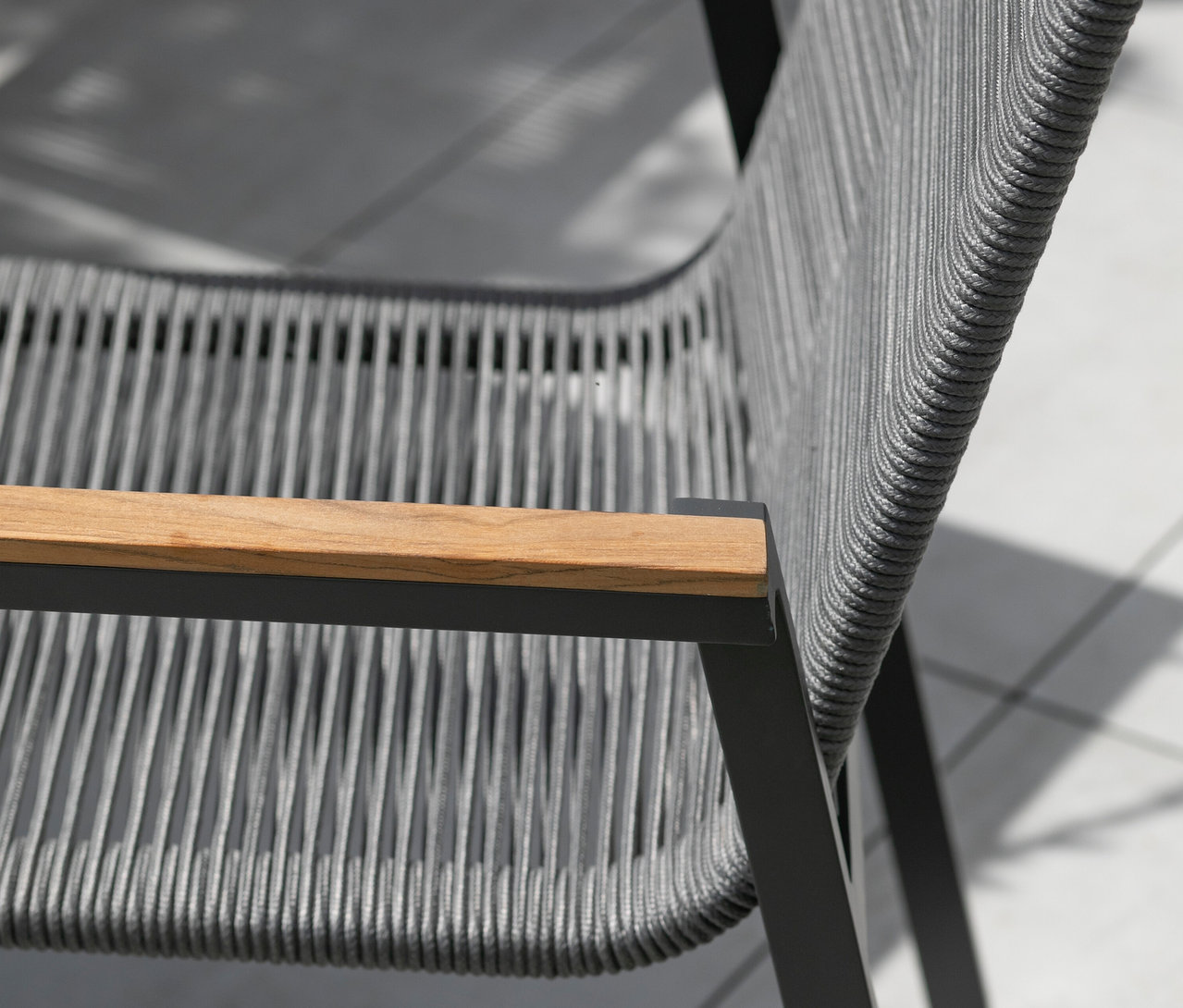 Nahaufnahme eines grauen Sessels mit Holzarmlehne auf einer Terrasse.