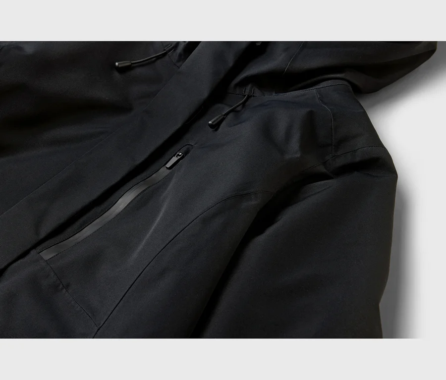 Nahaufnahme einer schwarzen Funktionsjacke mit Kapuze, mit einer diagonalen, versiegelten Reißverschlusstasche und Kordelzügen.