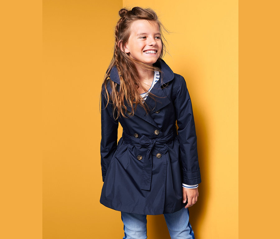 Lächelndes Mädchen posiert in einem dunkelblauen Allwetter-Trenchcoat.