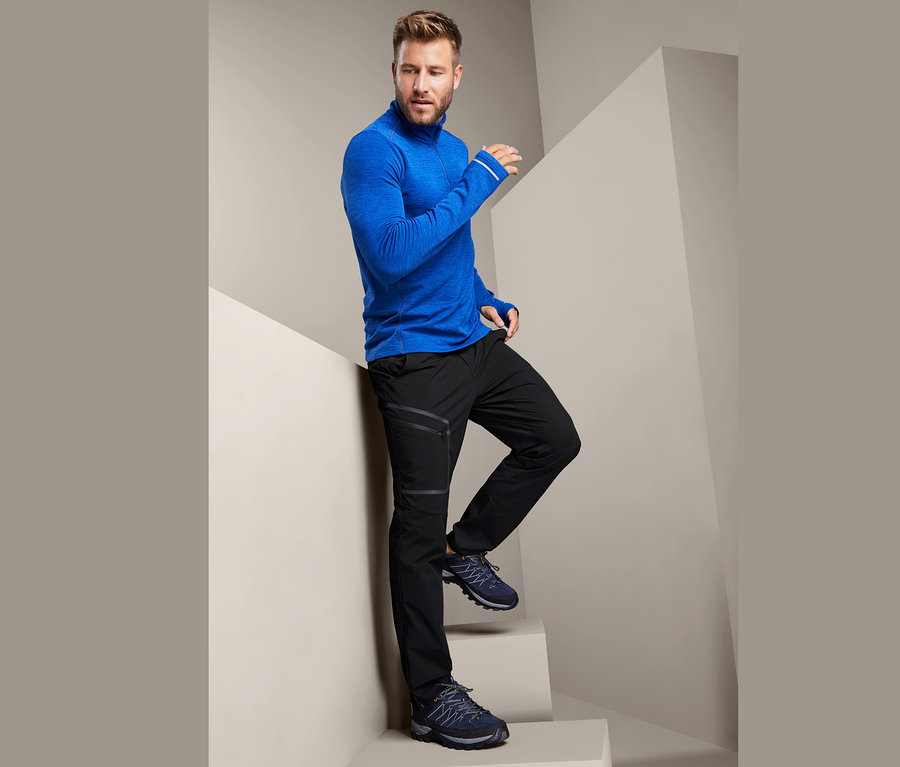 Mann posiert auf Treppen in einem blauen Funktionsshirt und einer schwarzen Softshellhose.