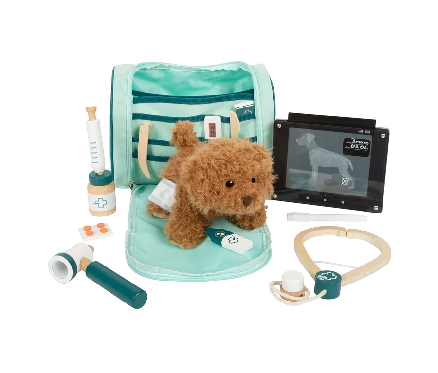Ein brauner Plüschhund liegt auf einer hellblauen Matte, umgeben von einem geöffneten small foot Tierarzt-Set »Hund«. Das Set enthält eine Spritze, Pillen, ein Stethoskop, einen Reflexhammer, ein Thermometer und ein Tablet mit Röntgenbild.