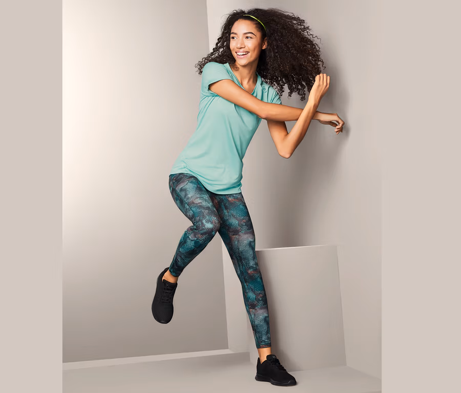 Lächelnde Frau posiert im Studio in Sporttight, T-Shirt und Turnschuhen.
