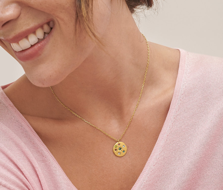 Detail einer lächelnden Frau mit einer Kette mit rundem Multicolor-Anhänger und Creolen mit Multicolor-Anhängern.