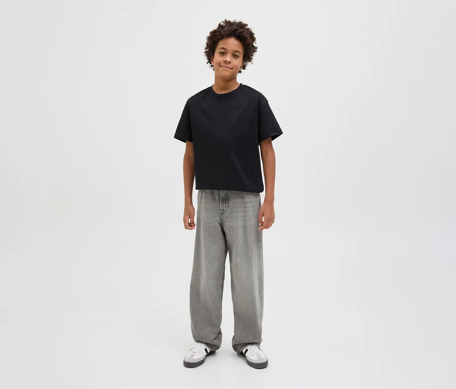 Ein Junge trägt ein schwarzes T-Shirt und graue Jack&Jones JJOrginial Alex Jeans.