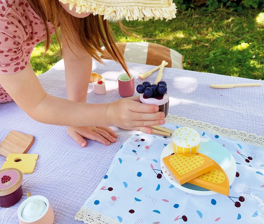 Kind spielt mit small foot Picknickkorb »tasty« auf einer Decke im Gras.