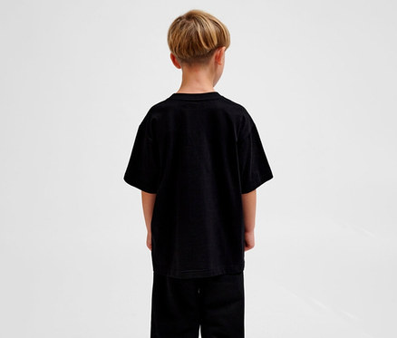 Junge von hinten, der ein schwarzes, locker geschnittenes hummel hmUR loose T-Shirt »Bee« und schwarze Hosen trägt.