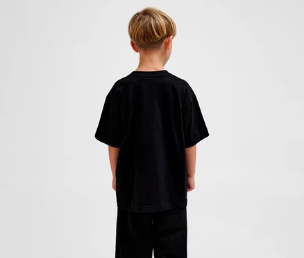 Junge von hinten, der ein schwarzes, locker geschnittenes hummel hmUR loose T-Shirt »Bee« und schwarze Hosen trägt.