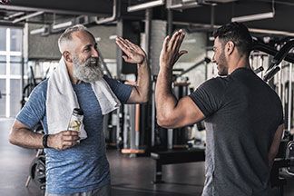 Gute Qualität bei Sportsocken und Sportschuhen: Ein jüngerer und ein älterer Mann, die beide Sportkleidung tragen und im Fitnessstudio stehen, klatschen sich gegenseitig ab.