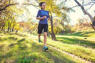 Eine Frau geht mit ihrem blauen Sportshirt im Wald joggen.