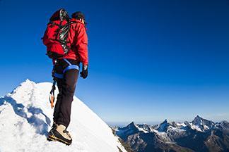 Ein Mann steht mit seiner Winter-Sporthose auf der Spitze eines Berges.