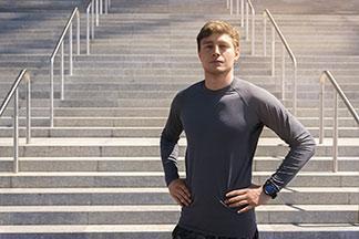 Ein Mann mit einem grauen Sportshirt steht vor einer Treppe.