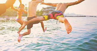 Sportbademode für jeden Typ: Eine Gruppe junger Männer und eine Frau springen ausgelassen ins Wasser.