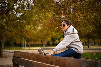 Eine junge Frau, die eine graue Fleecejacke trägt, dehnt sich bei herbstlichem Wetter an einer Parkbank.