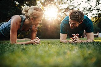 Ein Mann und eine Frau machen ohne Outdoor Fitnessgeräte Sport im Park und haben Spaß dabei.