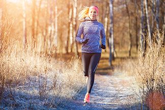 Laufen im Winter: Eine junge Frau, die ein Langarmshirt, ein Stirnband und lange Laufhosen trägt, joggt durch einen winterlichen Wald.