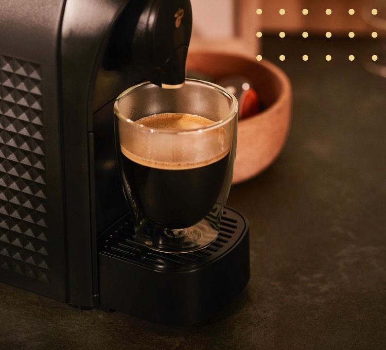 Stimmungsvolles Bild eines Glases Kaffee Crema unter einer Cafissimo Maschine